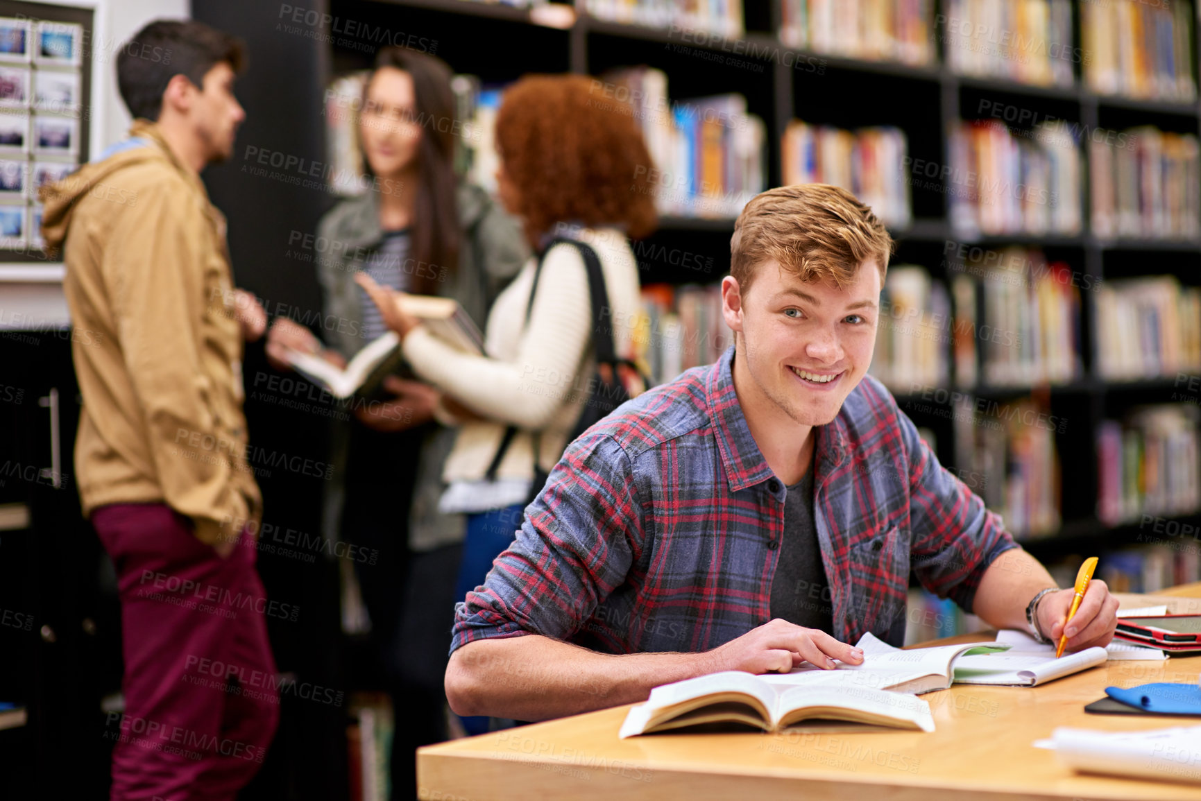 Buy stock photo Shot of a male student studying in a university library with his peers in the background