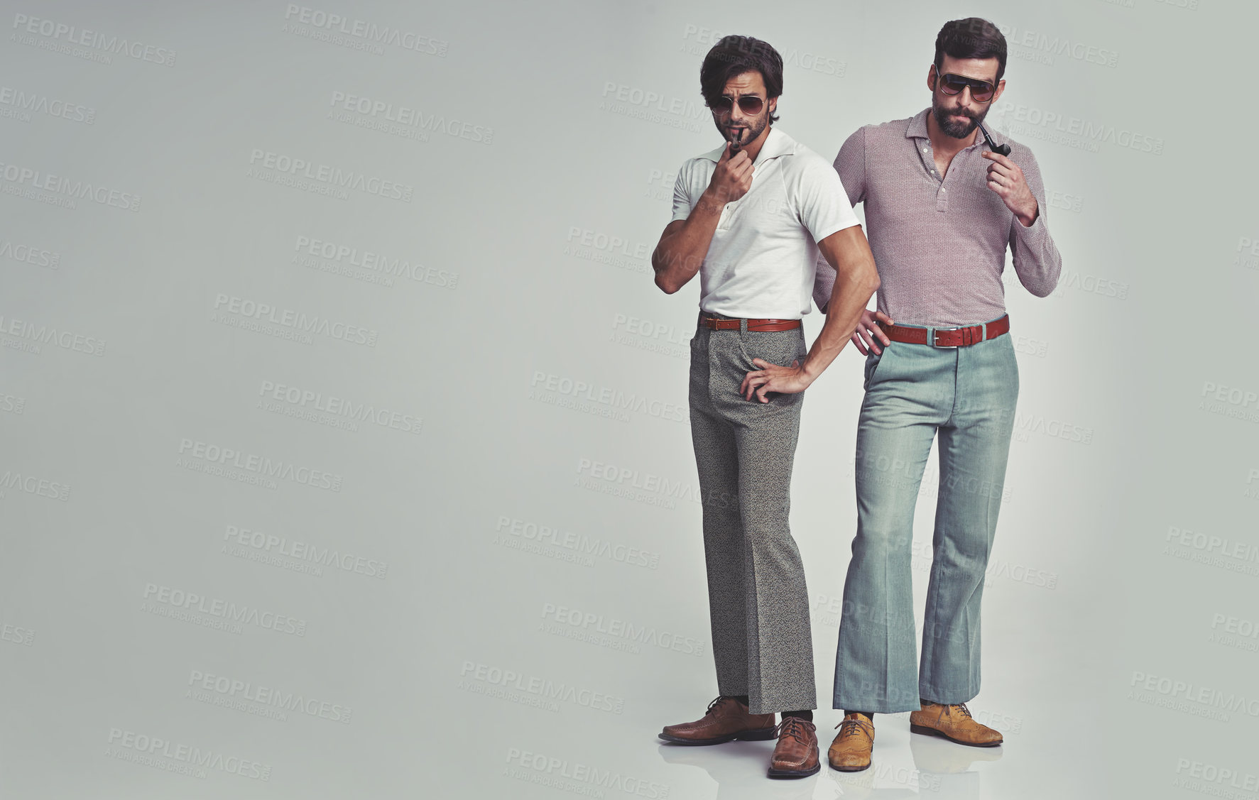 Buy stock photo Studio shot of two men standing together while wearing retro 70s wear and smoking pipes