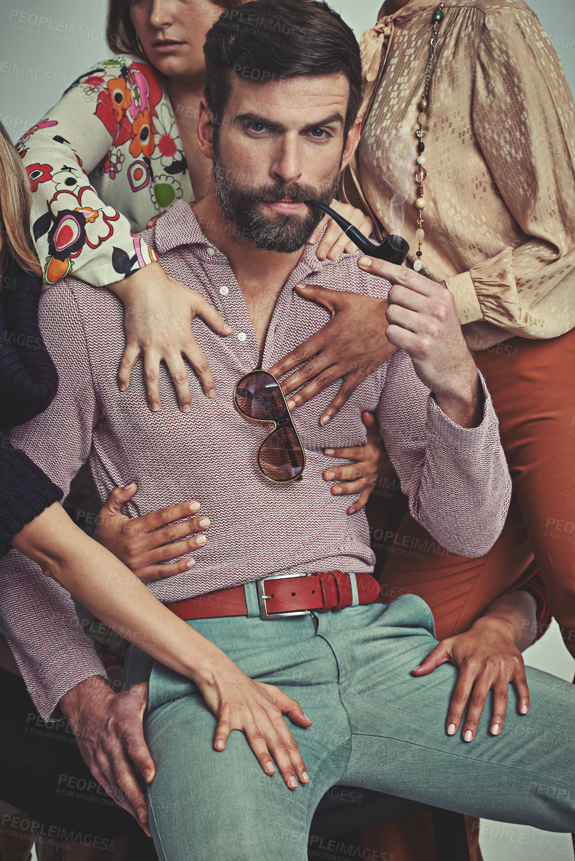 Buy stock photo Studio shot of an attractive man in retro 70s wear being touched by women while smoking his pipe
