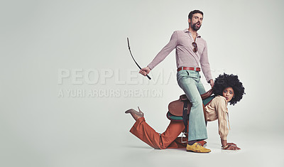 Buy stock photo A studio shot of an attractive man in 70s wear riding a young woman wearing a saddle while using a riding crop