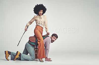 Buy stock photo A studio shot of an attractive woman in 70s wear riding a handsome man wearing a saddle while using a riding crop