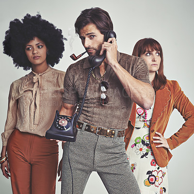 Buy stock photo Two attractive young hippies standing behind a handsome man using a retro telephone