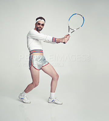 Buy stock photo A young man in the studio wearing ill-fitting retro tennis wear and shades while holding a racquetA young man in the studio wearing ill-fitting retro tennis wear and shades while holding a racquet