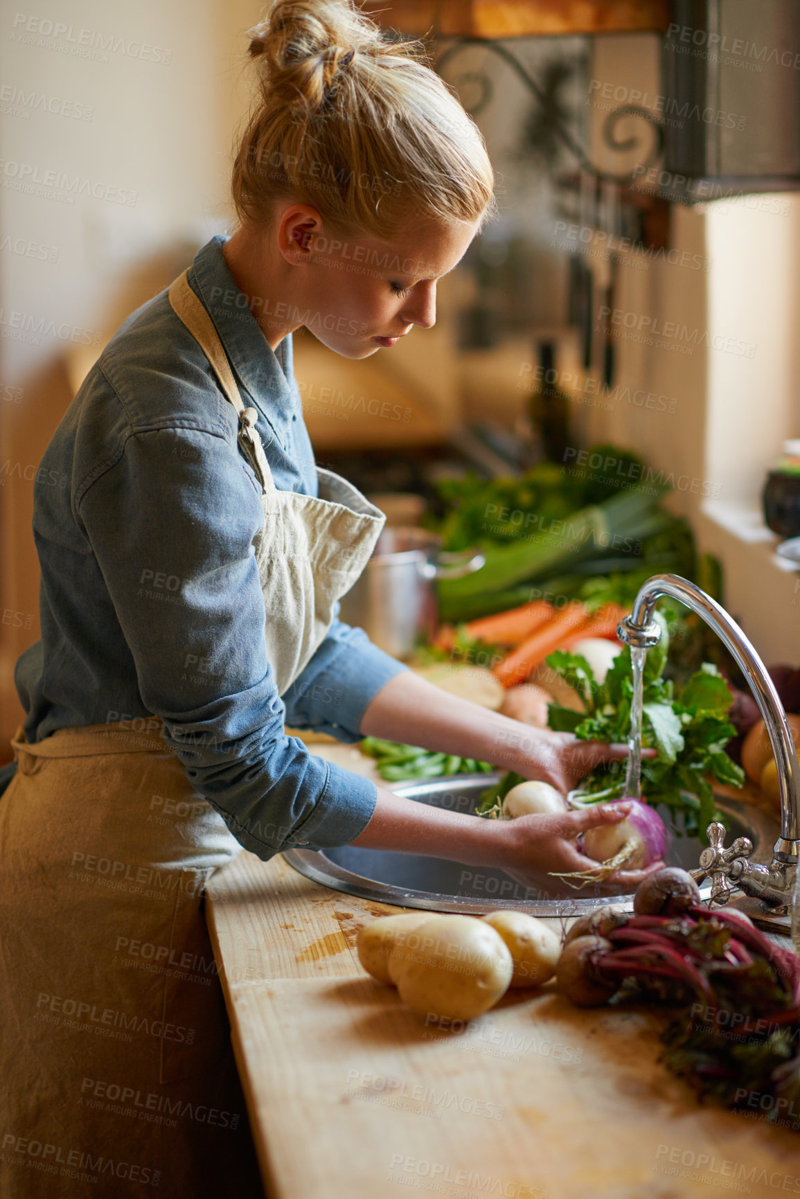 Buy stock photo Shot of a young woman  washing vegetables in a sink