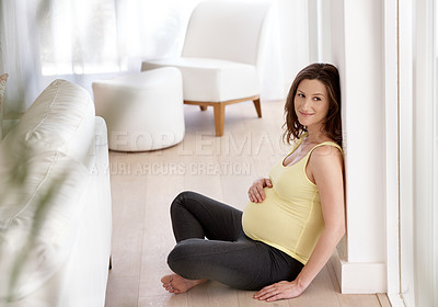 Buy stock photo Shot of a young pregnant woman sitting on her living room floor
