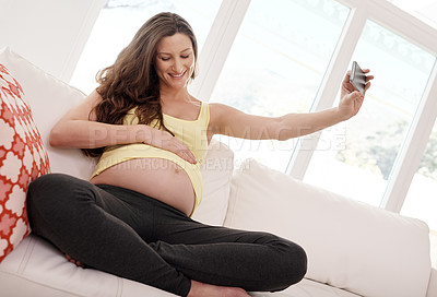 Buy stock photo Shot of a young pregnant woman taking a selfie with her cellphone in her living
