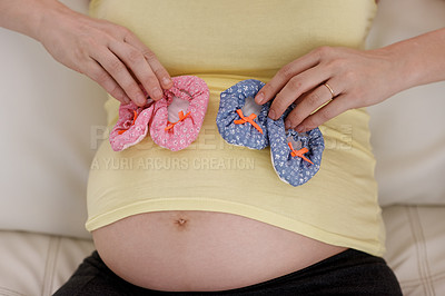 Buy stock photo Shot of a young pregnant woman holding a pair of pink and blue baby shoes against her belly