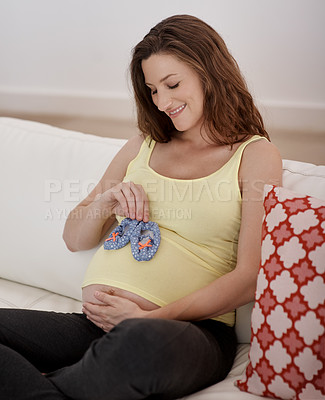 Buy stock photo Shot of a young pregnant woman holding a pair of blue baby shoes against her belly