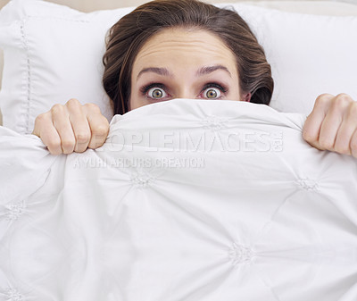 Buy stock photo A young woman peeking out from under her ned sheet with a frightened expression