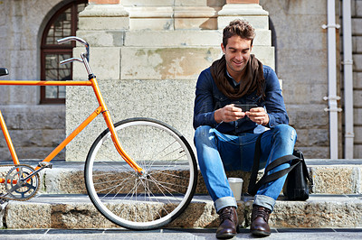 Buy stock photo Shot of a man using his cellphone while taking a break in the city with his bicycle beside him