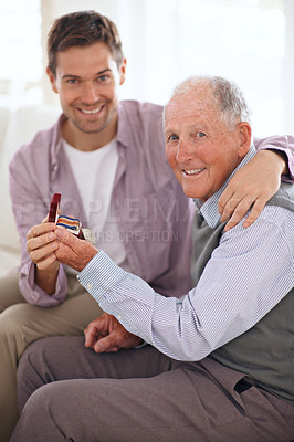 Buy stock photo Dad, adult son and medal for gift, support and congratulations with celebration and bonding at home. Men in portrait in lounge, family time with reward or award for present, happiness and gratitude