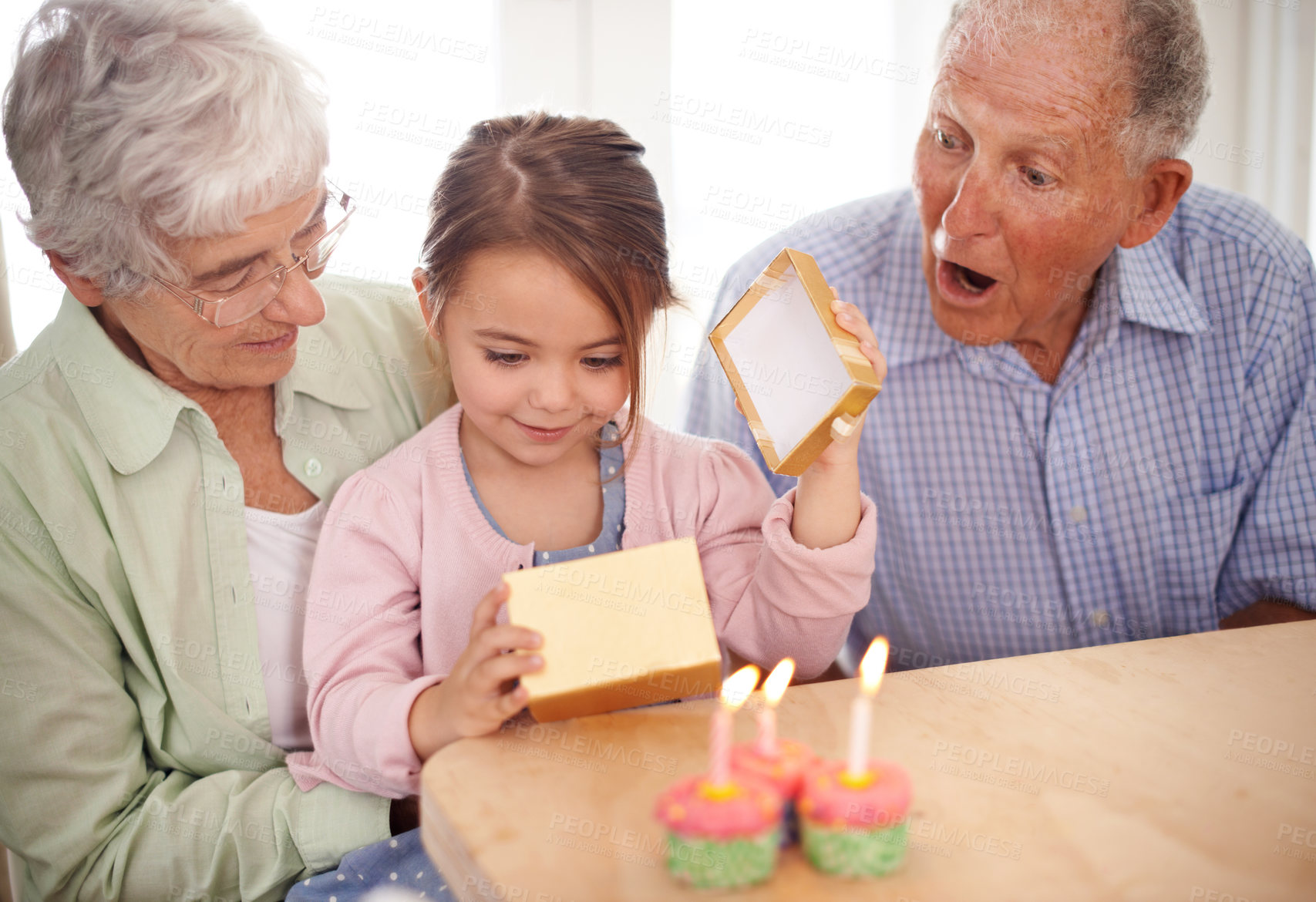 Buy stock photo Cupcakes, candles and girl with birthday, grandparents and gift with happiness, wow and home. Childhood, celebration and excited with dessert or present with party or box with omg, sweet or surprise