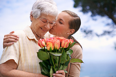 Buy stock photo Senior woman, daughter and kiss with flowers, hug and care for love, bonding and reunion at family home. People, elderly mom and mothers day celebration with connection, gift and bouquet in garden