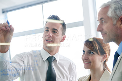 Buy stock photo Shot of businesspeople brainstorming on glass wall in an office