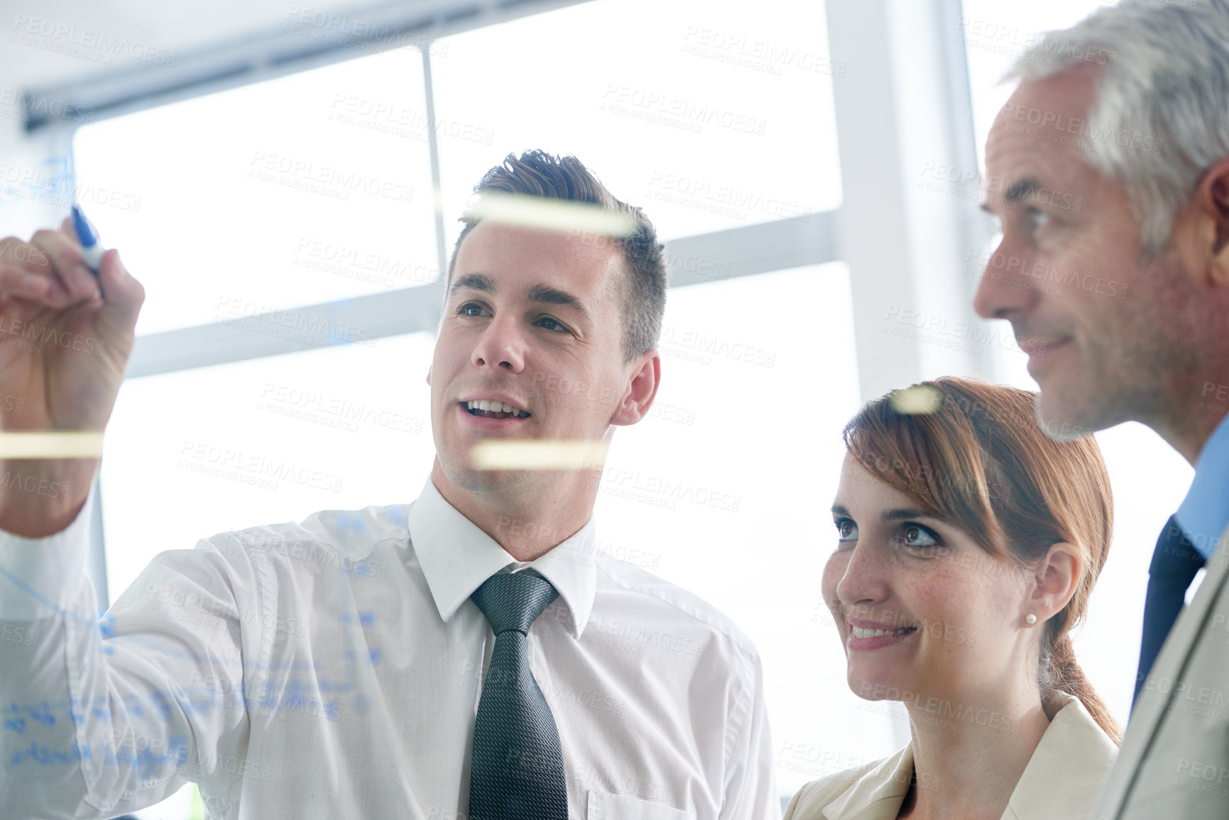 Buy stock photo Shot of businesspeople brainstorming on glass wall in an office