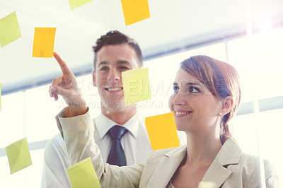 Buy stock photo Shot of a coworkers arranging sticky notes on a glass wall during a brainstorming session