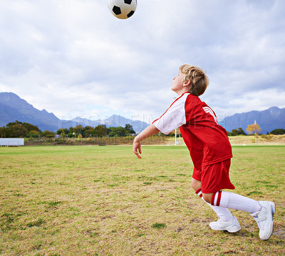 Buy stock photo Boy, soccer ball and playing on green grass for sports, training or practice with clouds and blue sky. Young football player, child or kid ready for kick off, game or match on outdoor field in nature