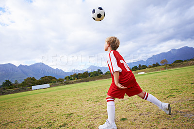 Buy stock photo Kid, soccer ball and playing on green grass for sports, training or practice with clouds and blue sky. Young football player or athlete ready for kick off, game or match on outdoor field in nature