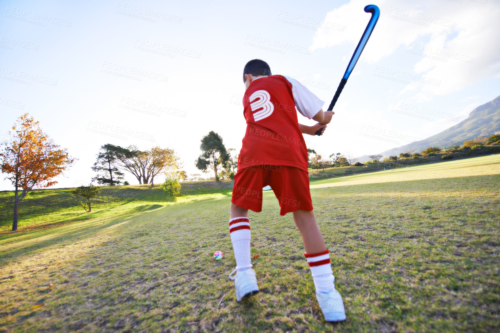 Buy stock photo Child, ball and hockey on green grass for game, sports or outdoor practice match in nature. Rear view of young kid or teen player enjoying day on field for fitness, activity or training with blue sky