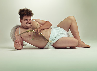 Buy stock photo Humor, cupid and portrait of man with costume in studio for wings, bow and arrow on gray background. Fantasy, love and plus size male model lying down for role play, creative dress up or cosplay