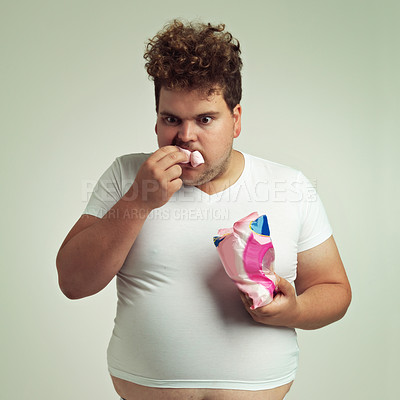 Buy stock photo Food, hungry and marshmallow with plus size man in studio on gray background for unhealthy eating. Hunger, appetite for sweets and ravenous young person with snack bag or packet for greed or gluttony