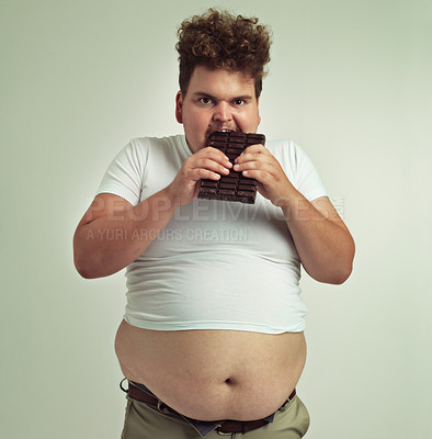 Buy stock photo Food, portrait and plus size man with chocolate, dessert and candy in a studio. Aggressive, sweet and unhealthy snack for over eating with funny face and hungry male person with green background