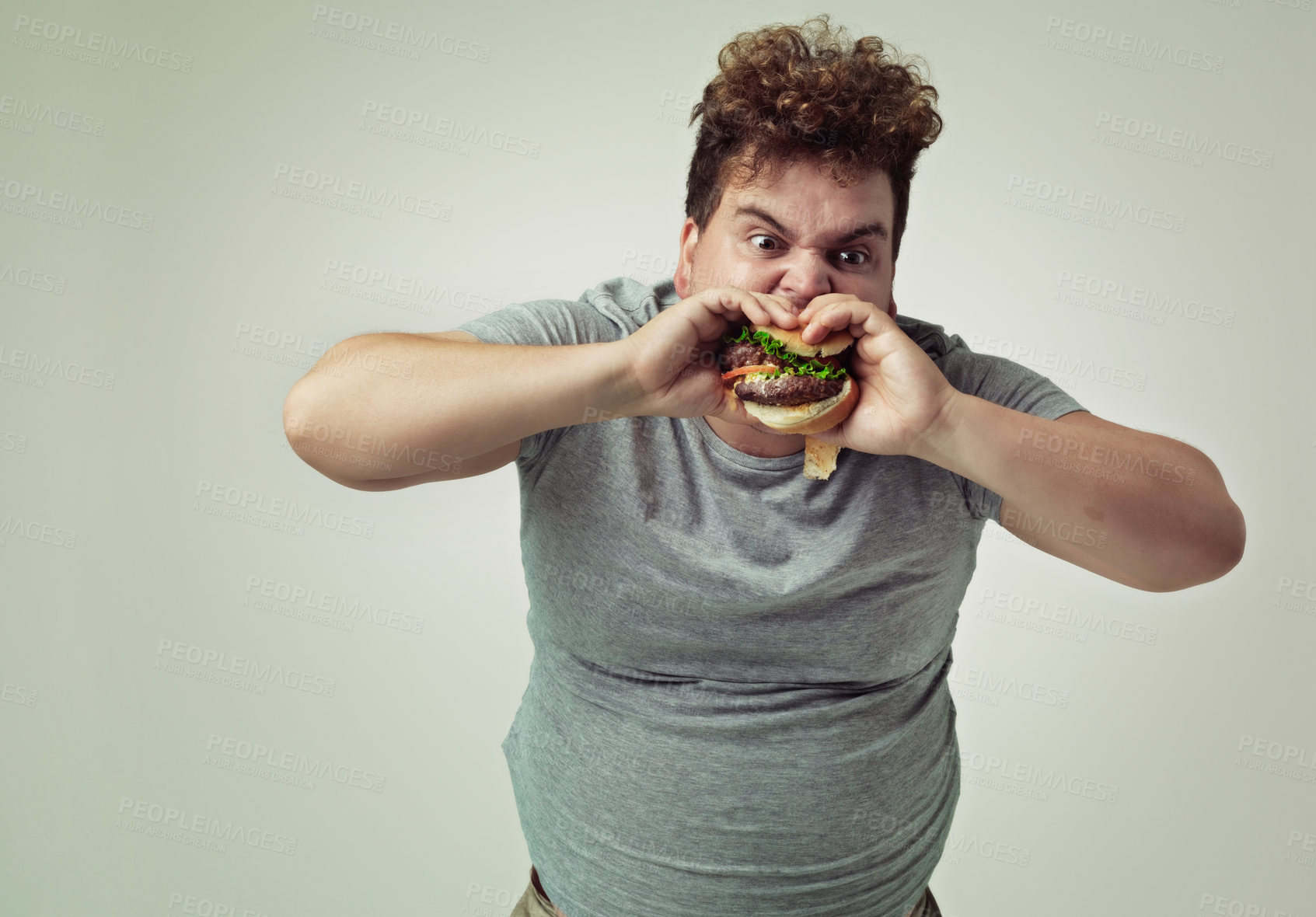 Buy stock photo Fast food, bite and man with hamburger in studio background for lunch, snack and craving of plus size person. Guy, sandwich or burger as takeaway meal for hunger, starving and eat while standing