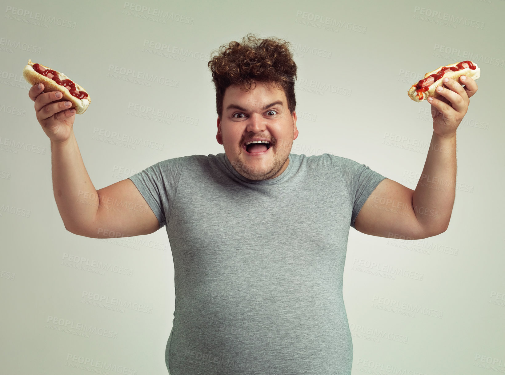 Buy stock photo Happy man, fast food and eating hotdog for lunch in studio background for snack, hunger and craving for plus size guy. Male person, hungry and takeaway meal for starving and enjoy while standing