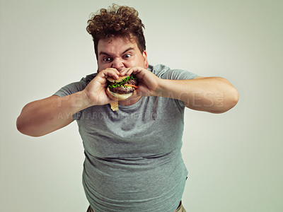 Buy stock photo Fast food, bite and person with hamburger in studio background for lunch, snack and craving of plus size guy. Overweight, man and burger or takeaway meal for hunger and eating while standing