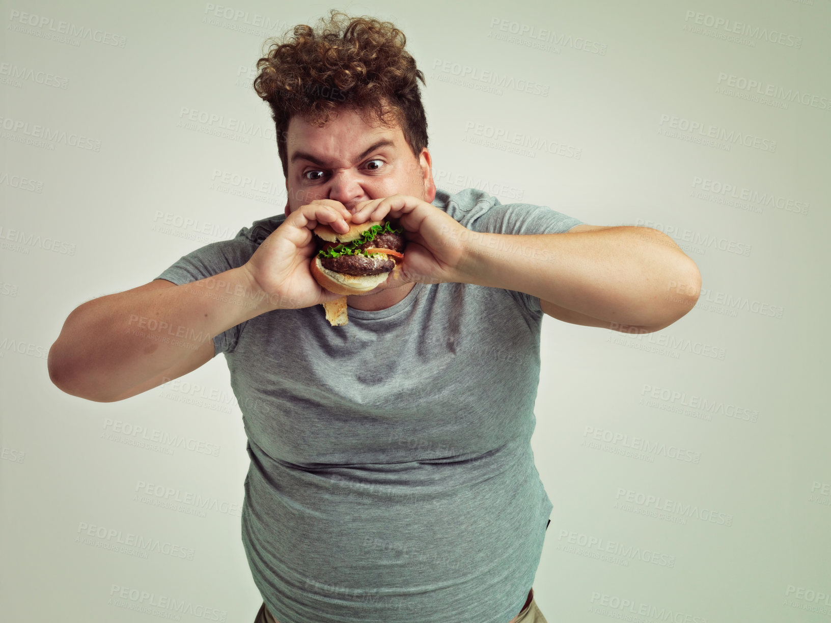 Buy stock photo Eating, plus size and man with hamburger in studio, hungry and bite of fast food with mouth. Male person, takeaway meal and snack for craving, starving and grilled sandwich by white background