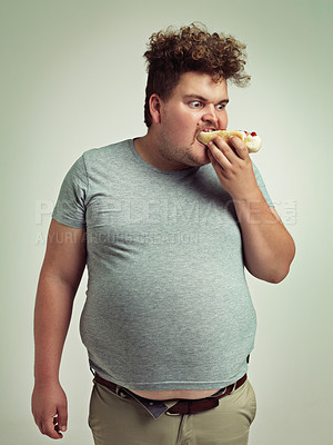 Buy stock photo Male person, fast food and eating hotdog for lunch in studio background for snack, hunger and craving for plus size guy. Man, hungry and burger or takeaway meal for starving and enjoy while standing