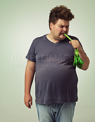 Buy stock photo Plus size, diet and disgusted man eating vegetable for health, nutrition and wellness in studio in white background. Weight loss, celery and unhappy male person for healthy food, wellbeing and detox