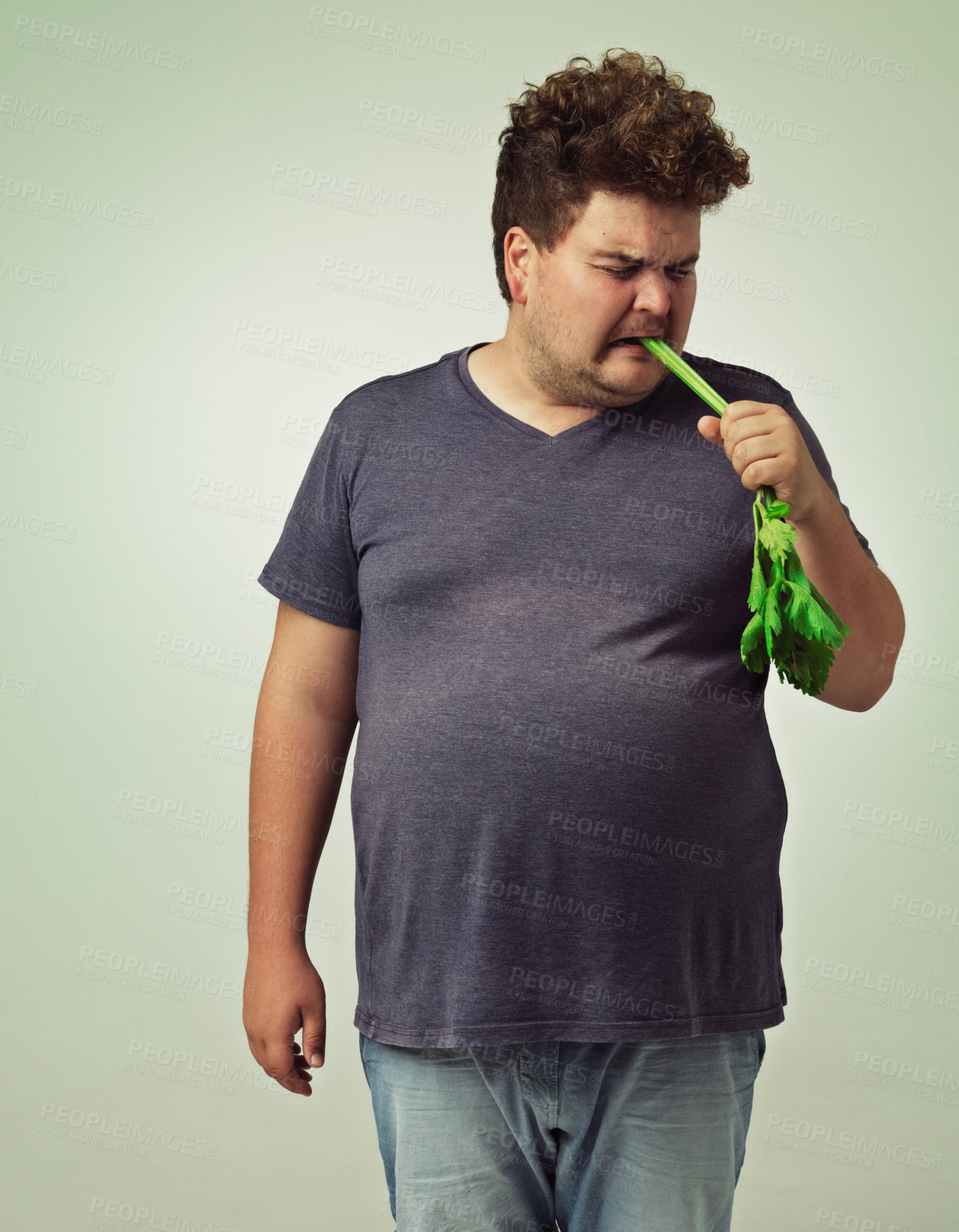 Buy stock photo Plus size, diet and disgusted man eating vegetable for health, nutrition and wellness in studio in white background. Weight loss, celery and unhappy male person for healthy food, wellbeing and detox