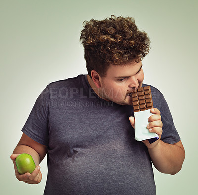 Buy stock photo Man, apple and chocolate in studio with choice of junk food, sweet or diet for wellness. Plus size, male person eating and decision, fruit or candy for nutrition, lose weight and healthy lifestyle