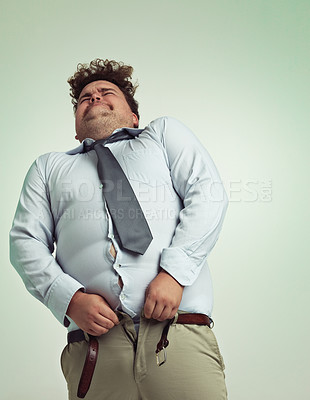 Buy stock photo Frustrated man, pants and plus size with big waist in obesity or overweight on a studio background. Young male person struggling to fit on clothing with body fat or chubby stomach on mockup space