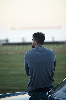 Buy stock photo Rearview shot of a man looking at the view while leaning against his car