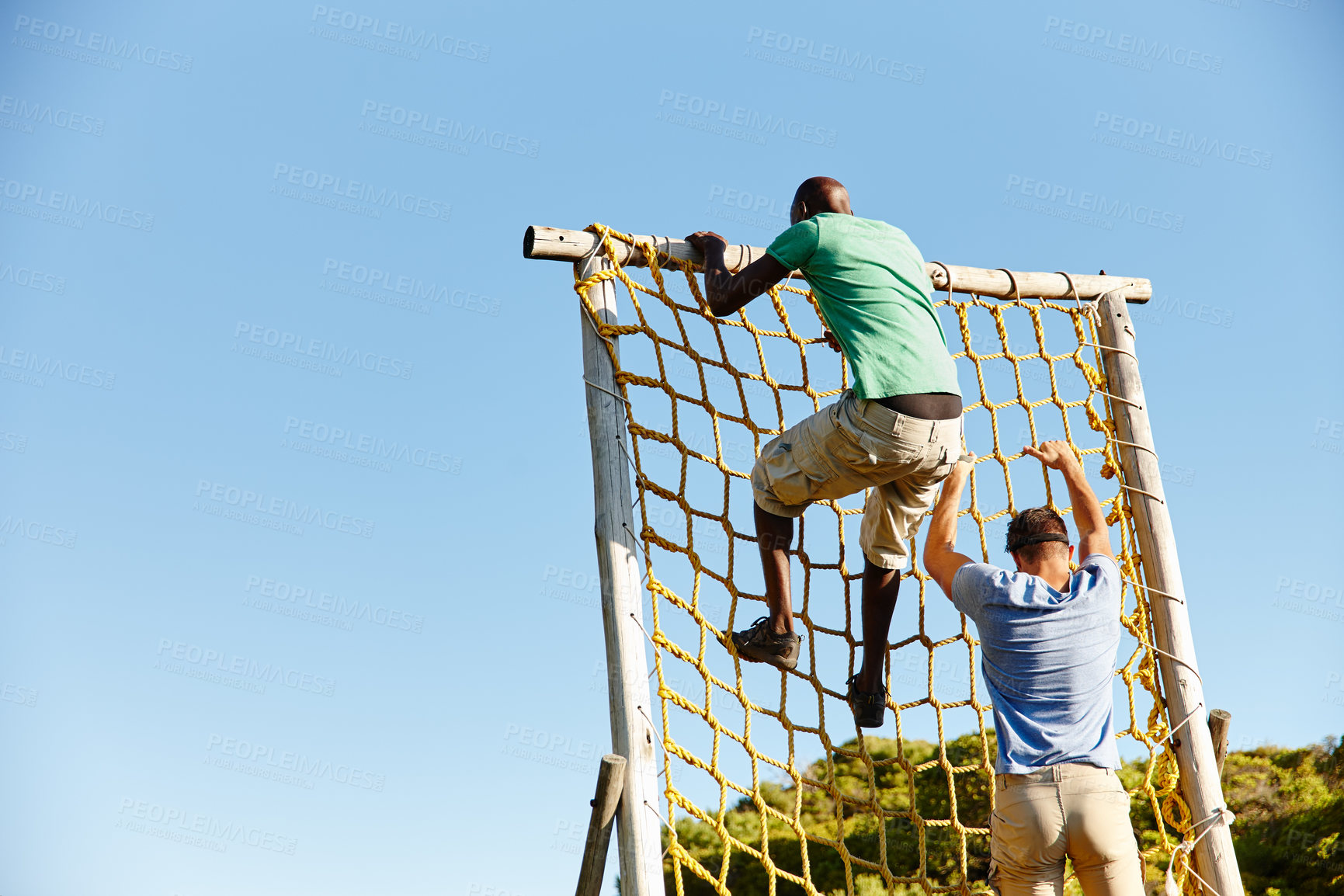 Buy stock photo Shot of two young men climbing over an obstacle at bootcamp