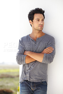 Buy stock photo Shot of a handsome young man leaning against a wall with his arms crossed