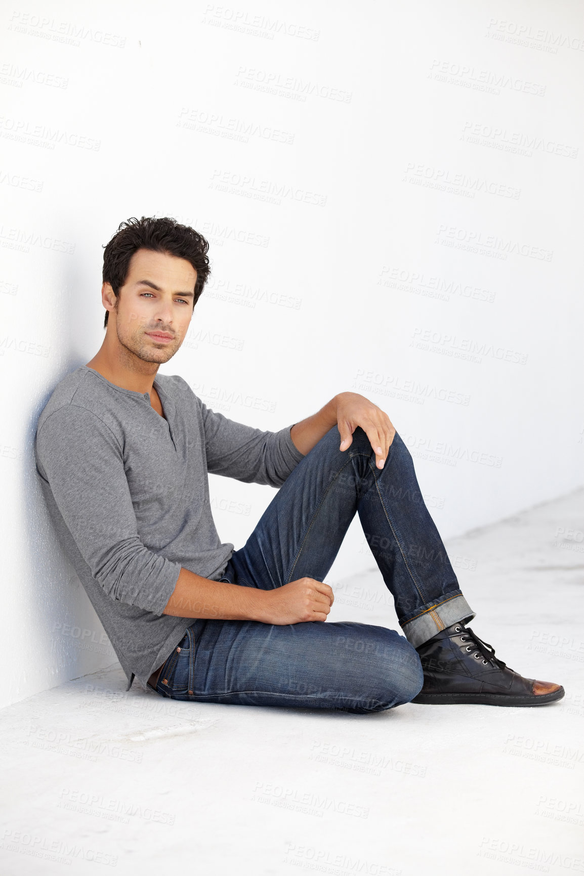 Buy stock photo Shot of a handsome young man sitting on the floor leaning against a white wall