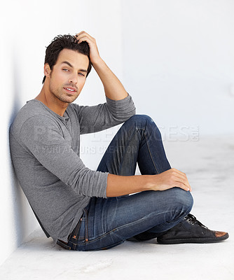 Buy stock photo Shot of a handsome young man sitting on the floor leaning against a white wall