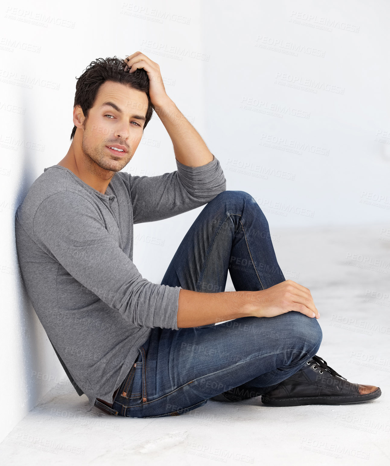 Buy stock photo Shot of a handsome young man sitting on the floor leaning against a white wall