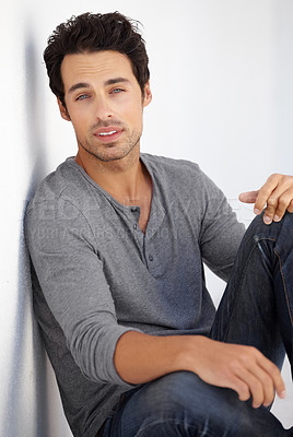 Buy stock photo Cropped portrait of a handsome young man sitting on the floor leaning against a white wall