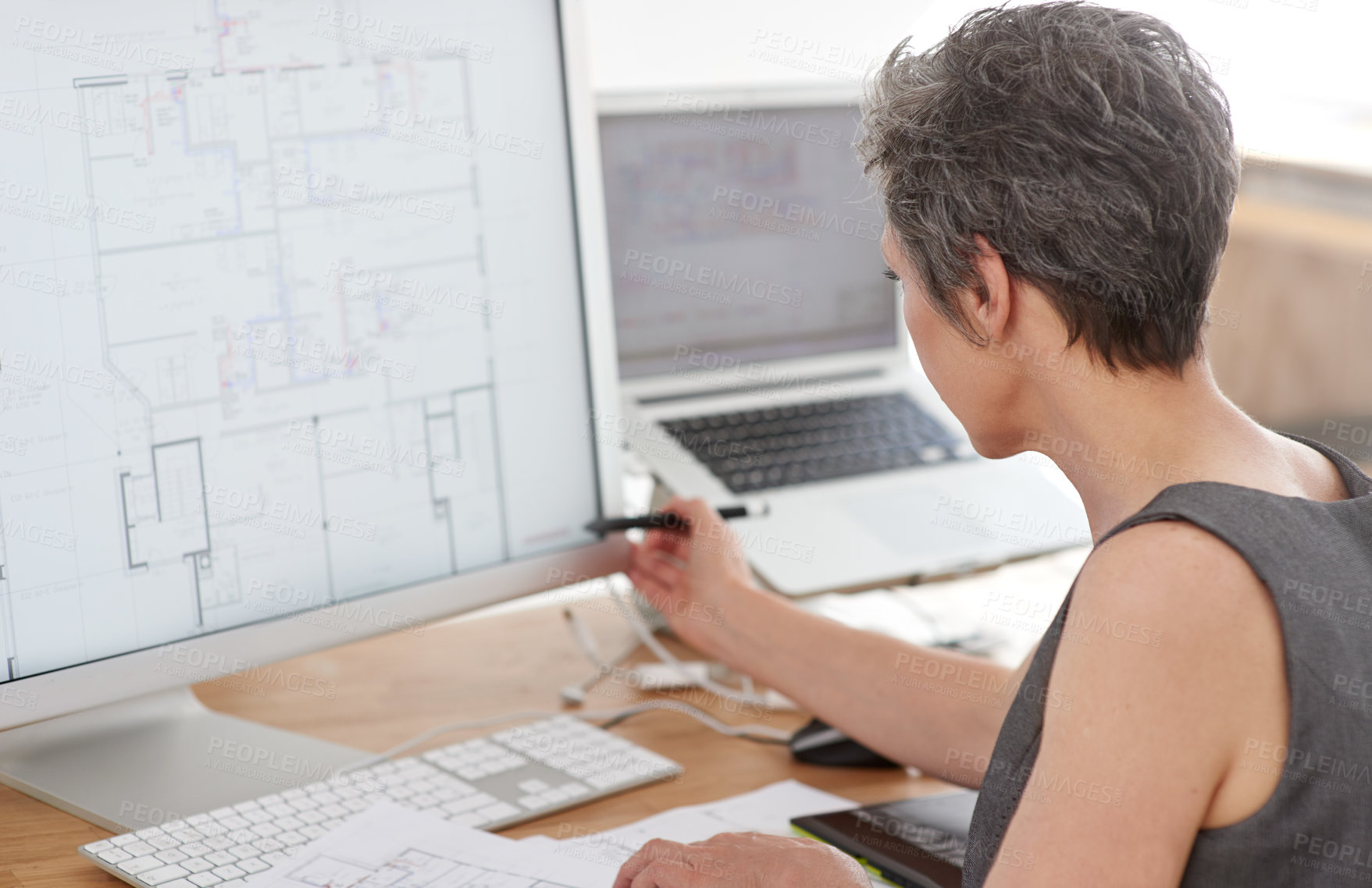 Buy stock photo A mature female architect working on building plans on her touchscreen computer