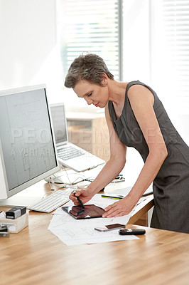 Buy stock photo Shot of a mature female architect working on blueprints in her office