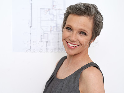 Buy stock photo Portrait of a mature female architect standing in front of a wall with building plans on it