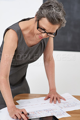 Buy stock photo Shot of a mature female architect going over building plans in her office