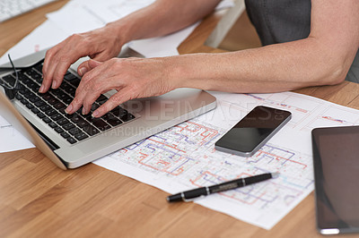 Buy stock photo Cropped image of an architect working on her laptop with building plans beside her on her desk