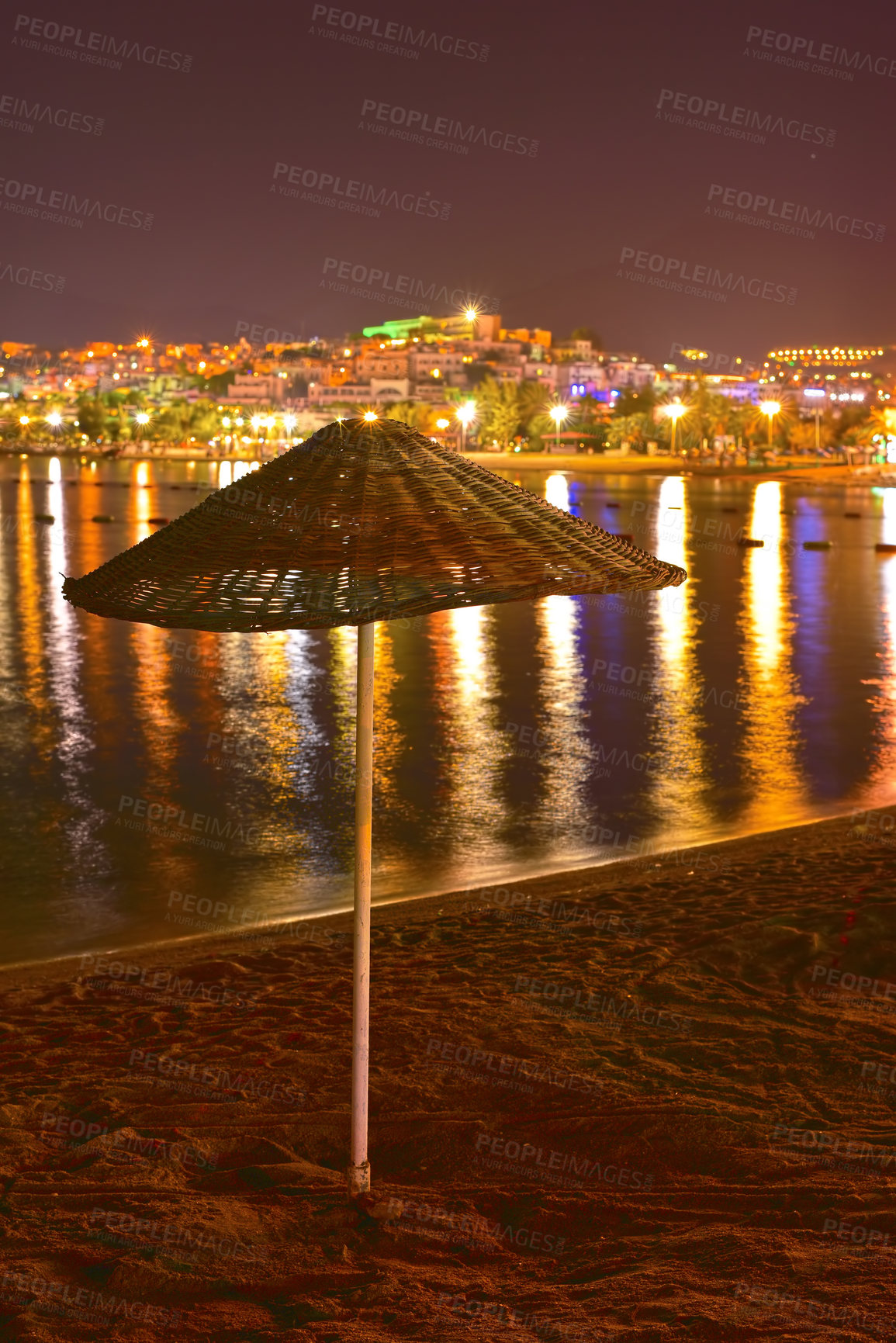 Buy stock photo Umbrella, beach and night with city lights, reflection and vacation with adventure, travel and getaway trip. Empty, evening and nature with water, sand and holiday with journey, dark and environment