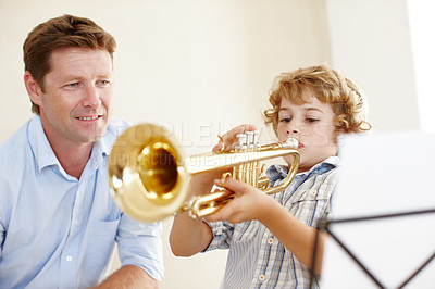 Buy stock photo Shot of a cute little boy playing the trumpet  while his father watches him proudly