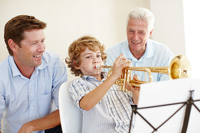 Buy stock photo Shot of a cute little boy playing the trumpet  while his father and grandfather watch him proudly